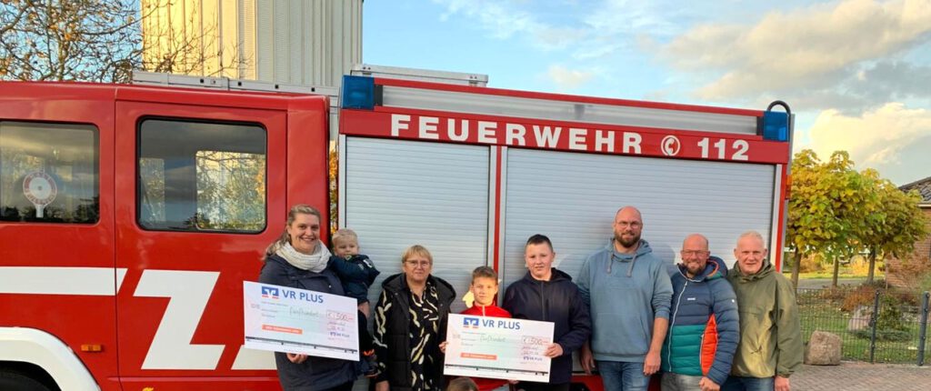 Feuerwehrauto mit 6 Personen davor, die einen Scheck zeigen