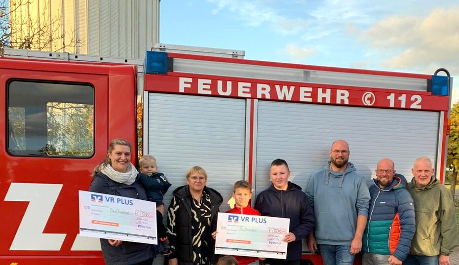 Feuerwehrauto mit 6 Personen davor, die einen Scheck zeigen